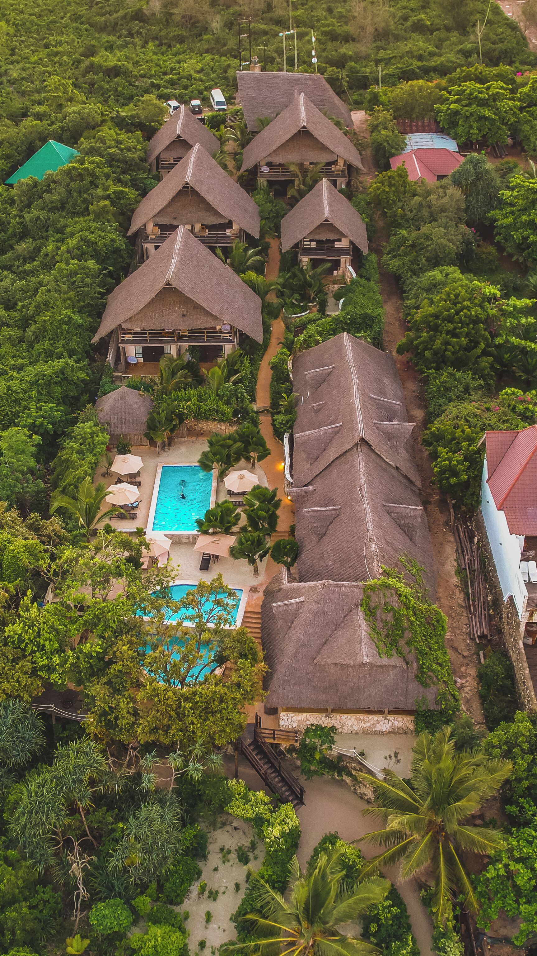 A resort with multiple thatched-roof cottages, a central swimming pool, and lush greenery surrounding the property.
