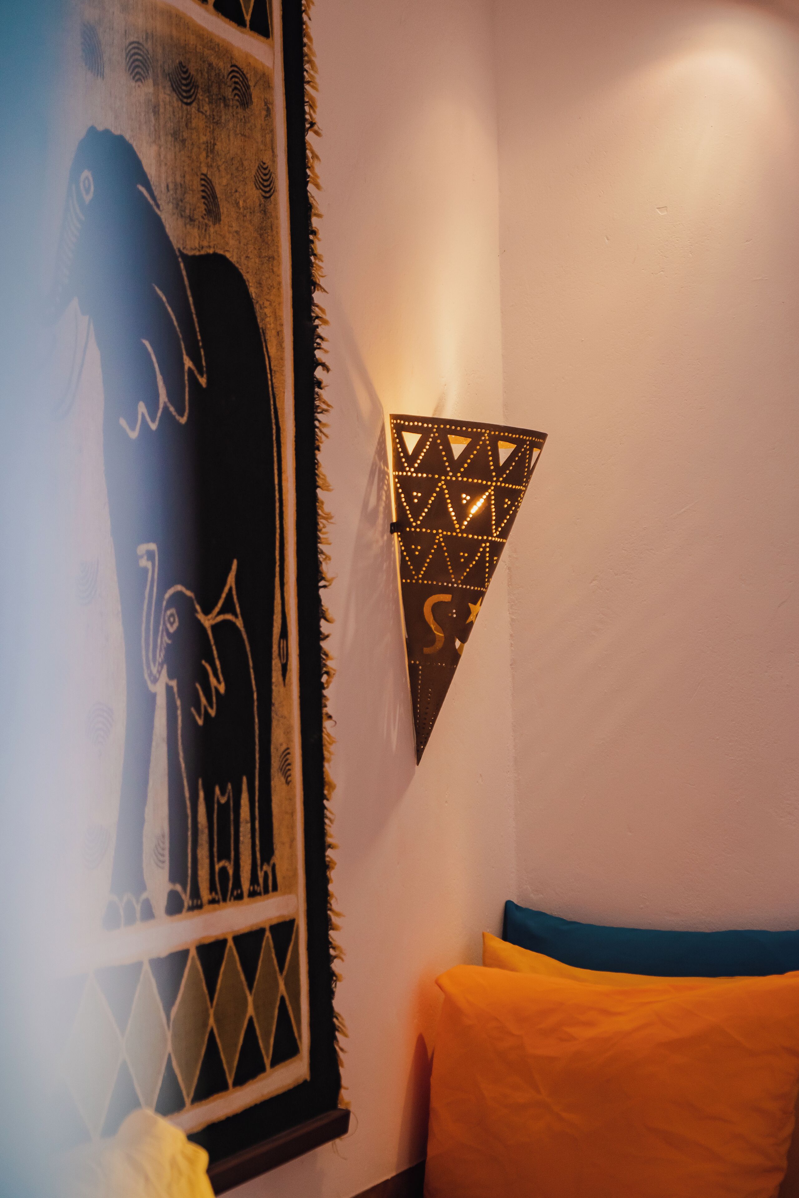 Una habitació amb un llit, una paret amb un llum geomètric i una finestra amb un disseny decoratiu.