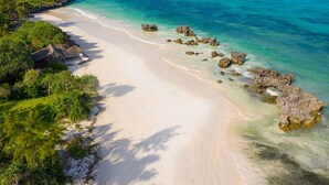 A beach with clear turquoise water, white sand, and scattered rocks. - Sunshine Bay Zanzibar - Adult Only (Matemwe)