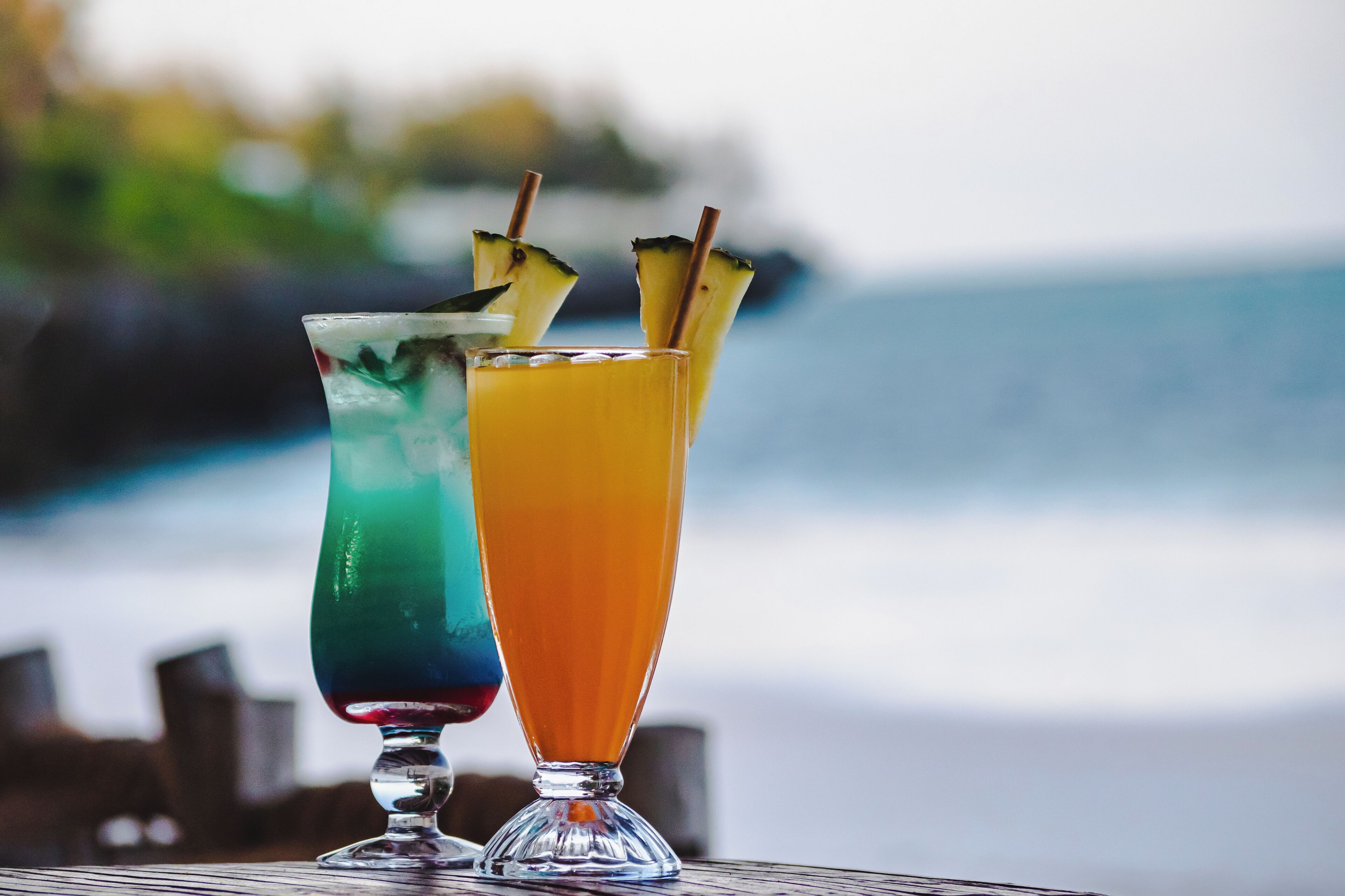 Two cocktails on a table with a blurred beach and ocean in the background.