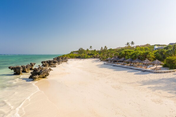 A beach with clear turquoise water, white sand, and thatched-roof beach huts. - Sunshine Bay Zanzibar - Adult Only (Matemwe)