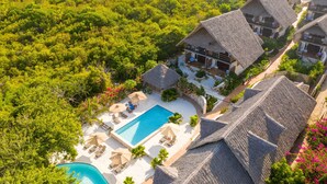 An aerial view of a resort with thatched-roof buildings, a swimming pool, and lush greenery. - Sunshine Bay Zanzibar - Adult Only (Matemwe)
