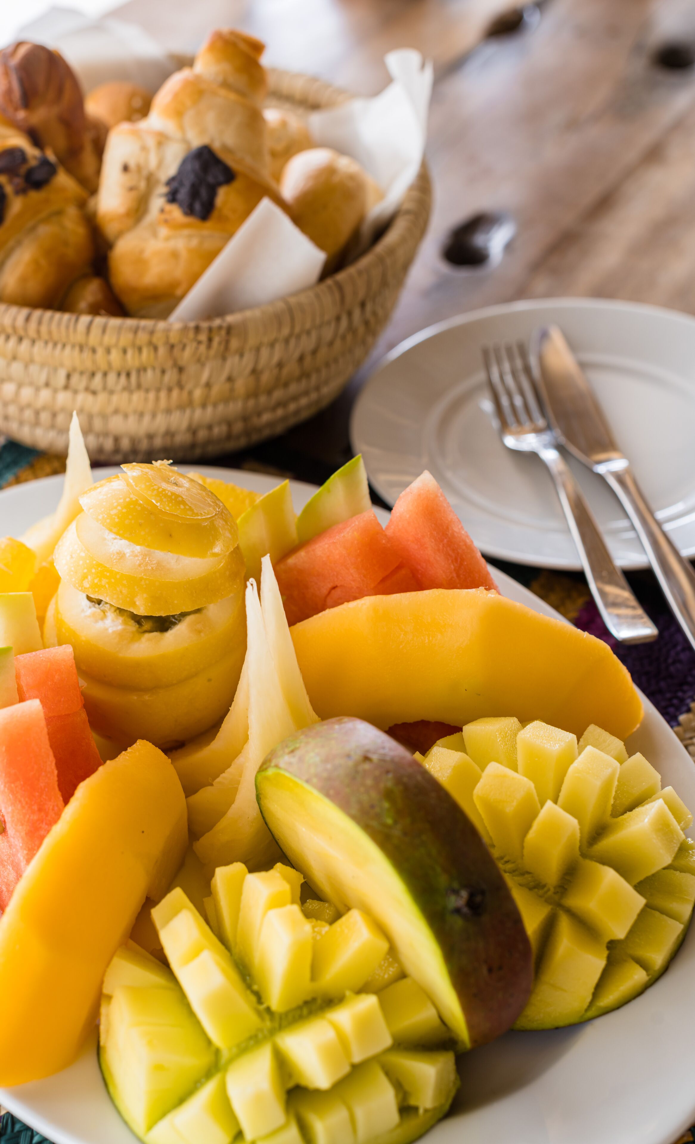 A plate of sliced fruits and a basket of pastries.
