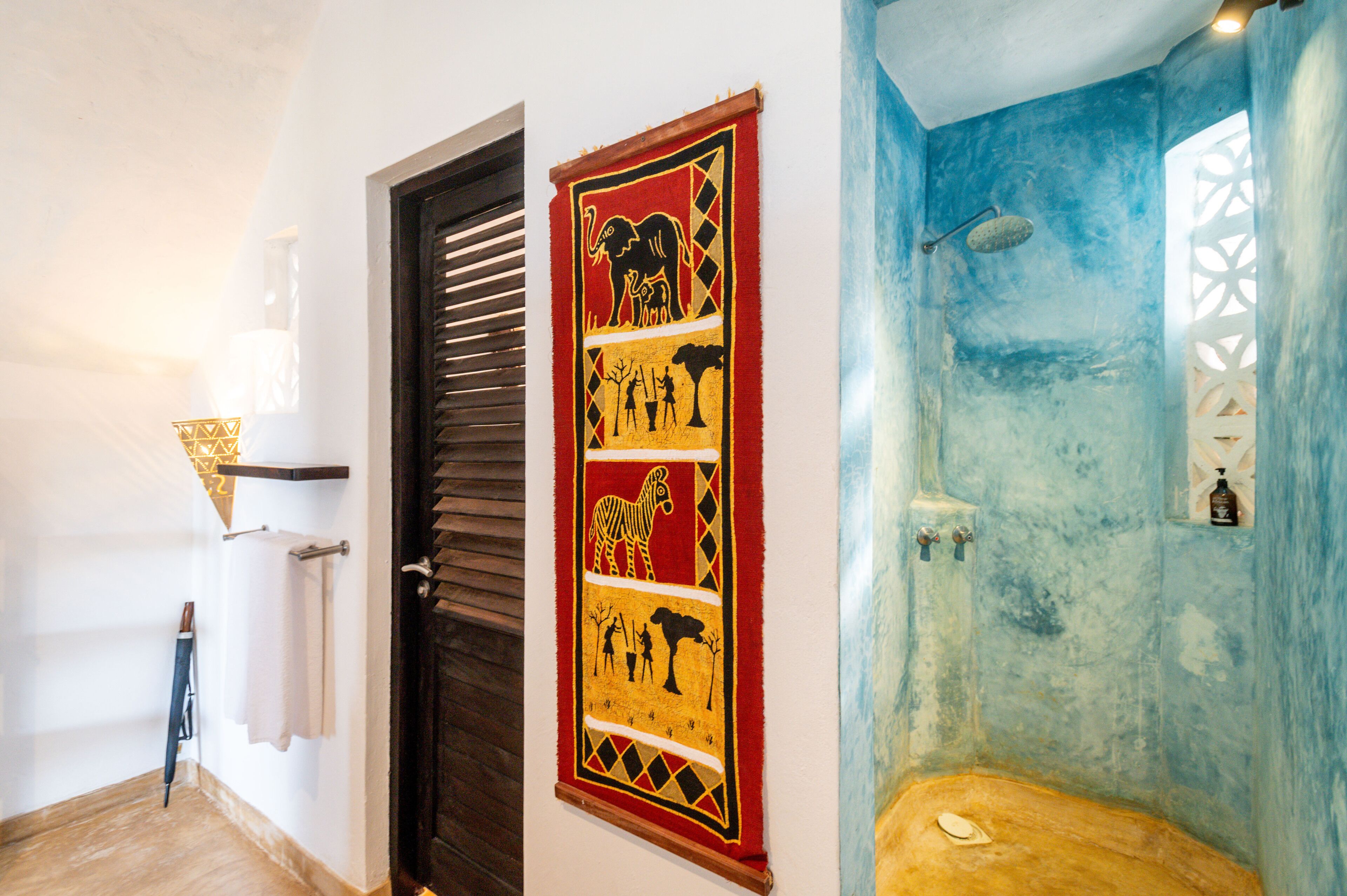 Une salle de bain avec un mur bleu, une douche et une tapisserie décorative représentant des silhouettes d’animaux et d’arbres.