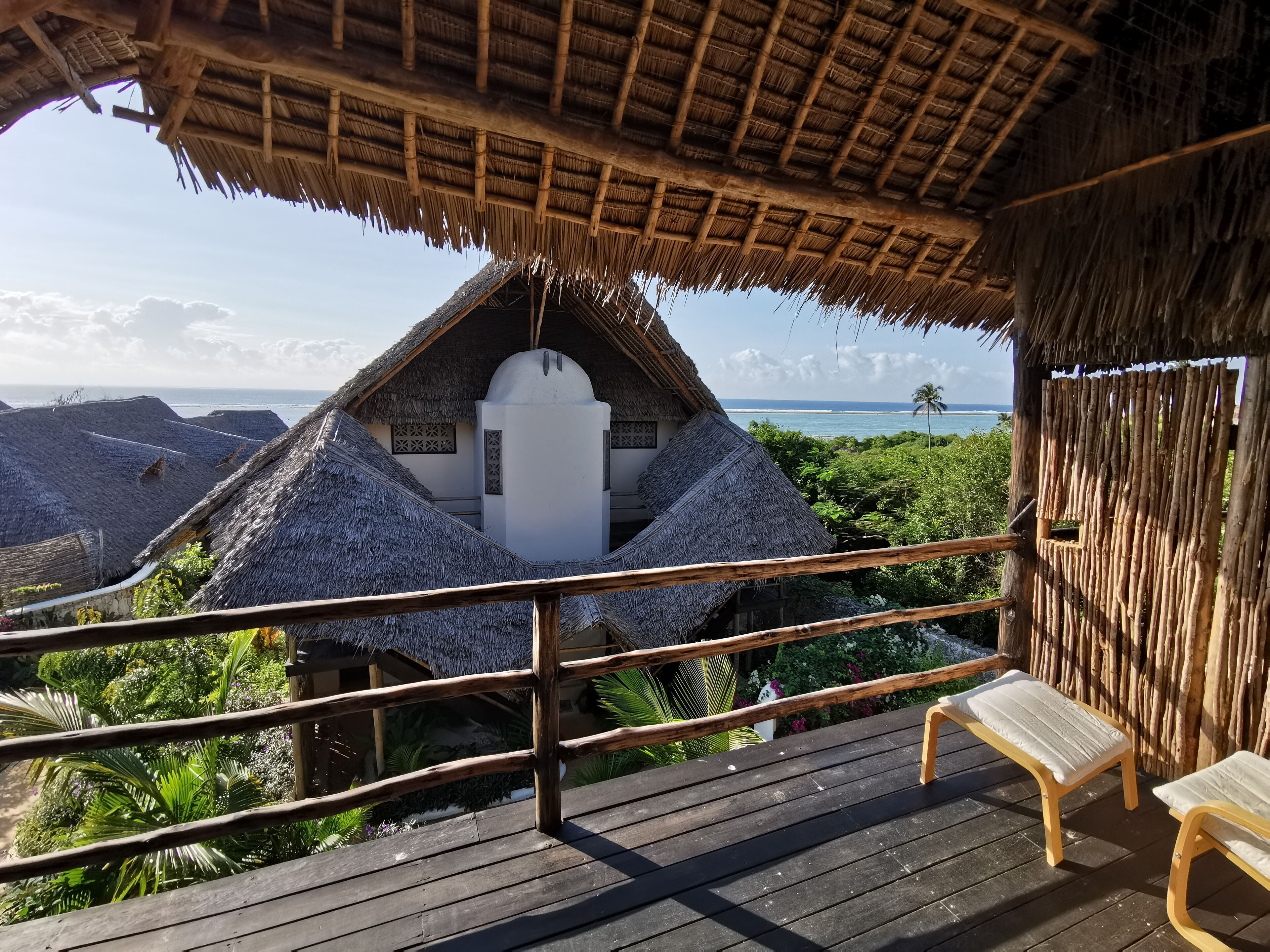 Una estructura con techo de paja, un balcón, barandas de madera y vista al océano.
