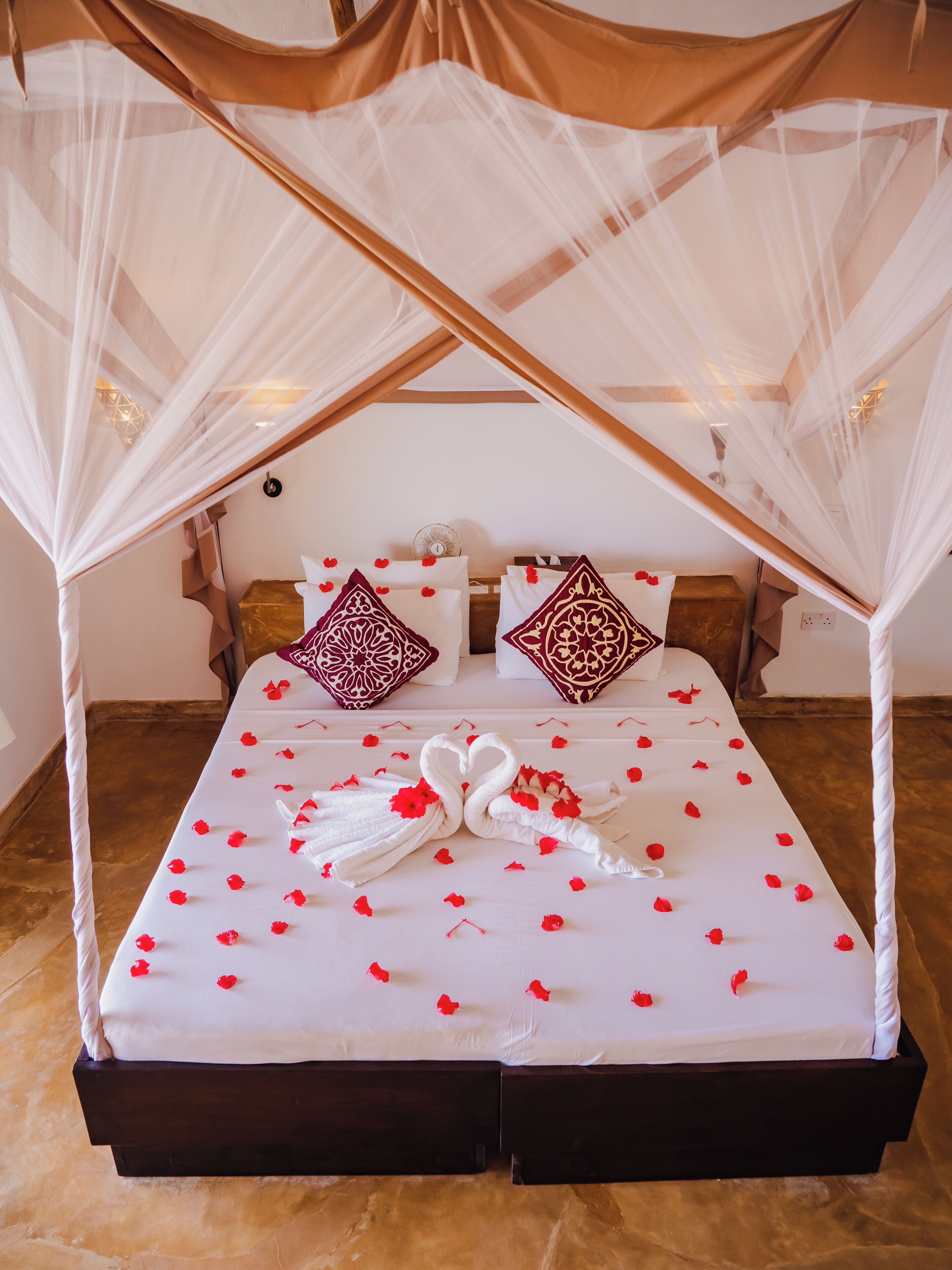A bed with a canopy, white bedding, and red rose petals.