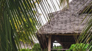 A thatched-roof structure with a stone wall and wooden railing, surrounded by lush greenery. - Sunshine Bay Zanzibar - Adult Only (Matemwe)
