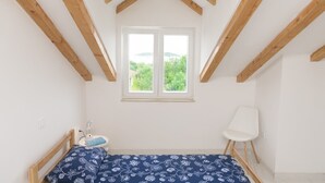 Un dormitorio con techo de madera, una cama con colcha floral, una mesita de noche con lámpara, una silla y una ventana con vistas a la vegetación.