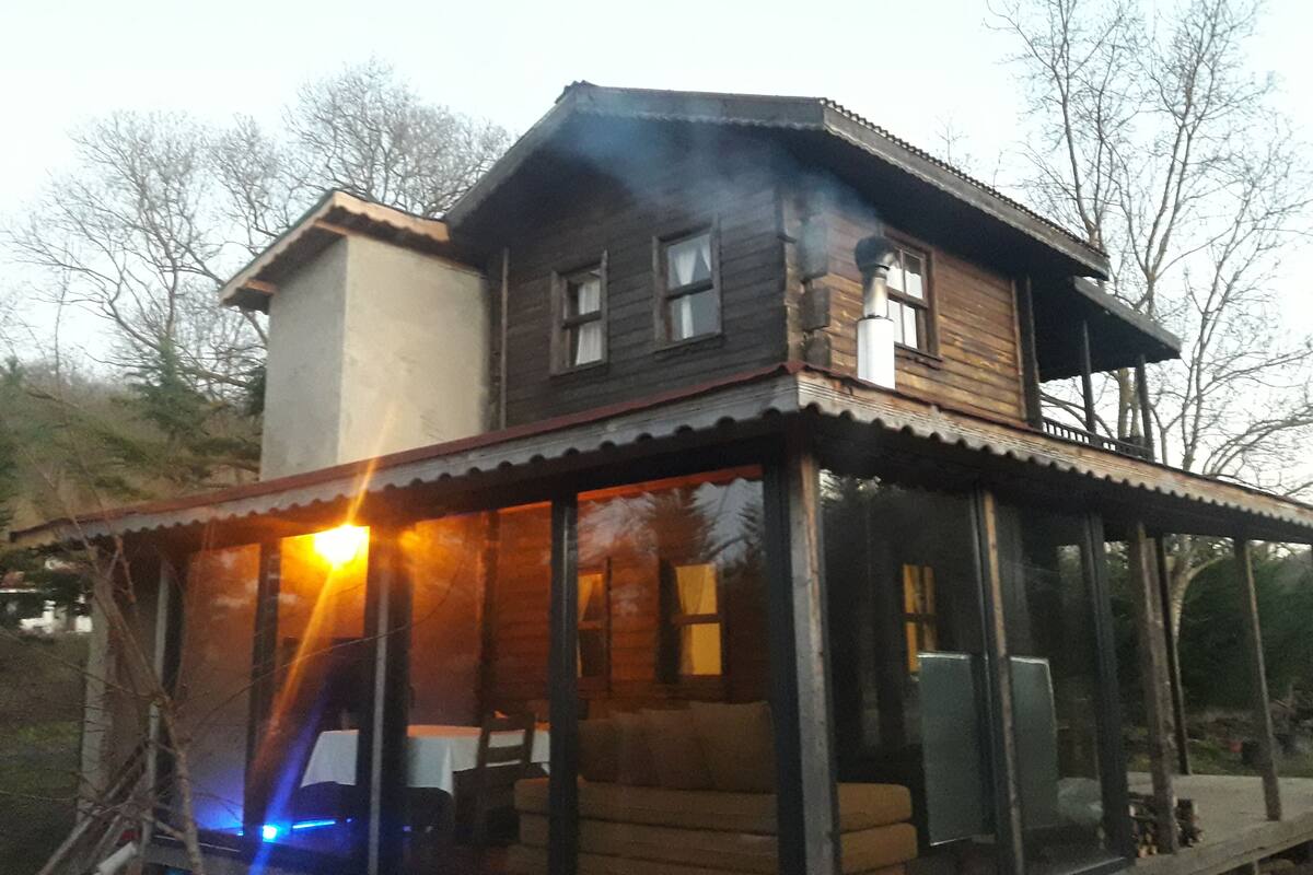 Uma casa de madeira de dois andares com varanda e chaminé soltando fumaça.