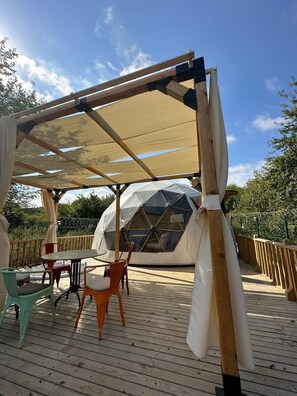 Une structure en forme de dôme géodésique dotée d’une terrasse en bois et d’un espace de détente extérieur.