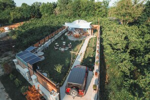 Vue aérienne d’une maison moderne dotée d’une grande structure en forme de dôme, d’un panneau solaire et d’un véhicule garé dans l’allée.