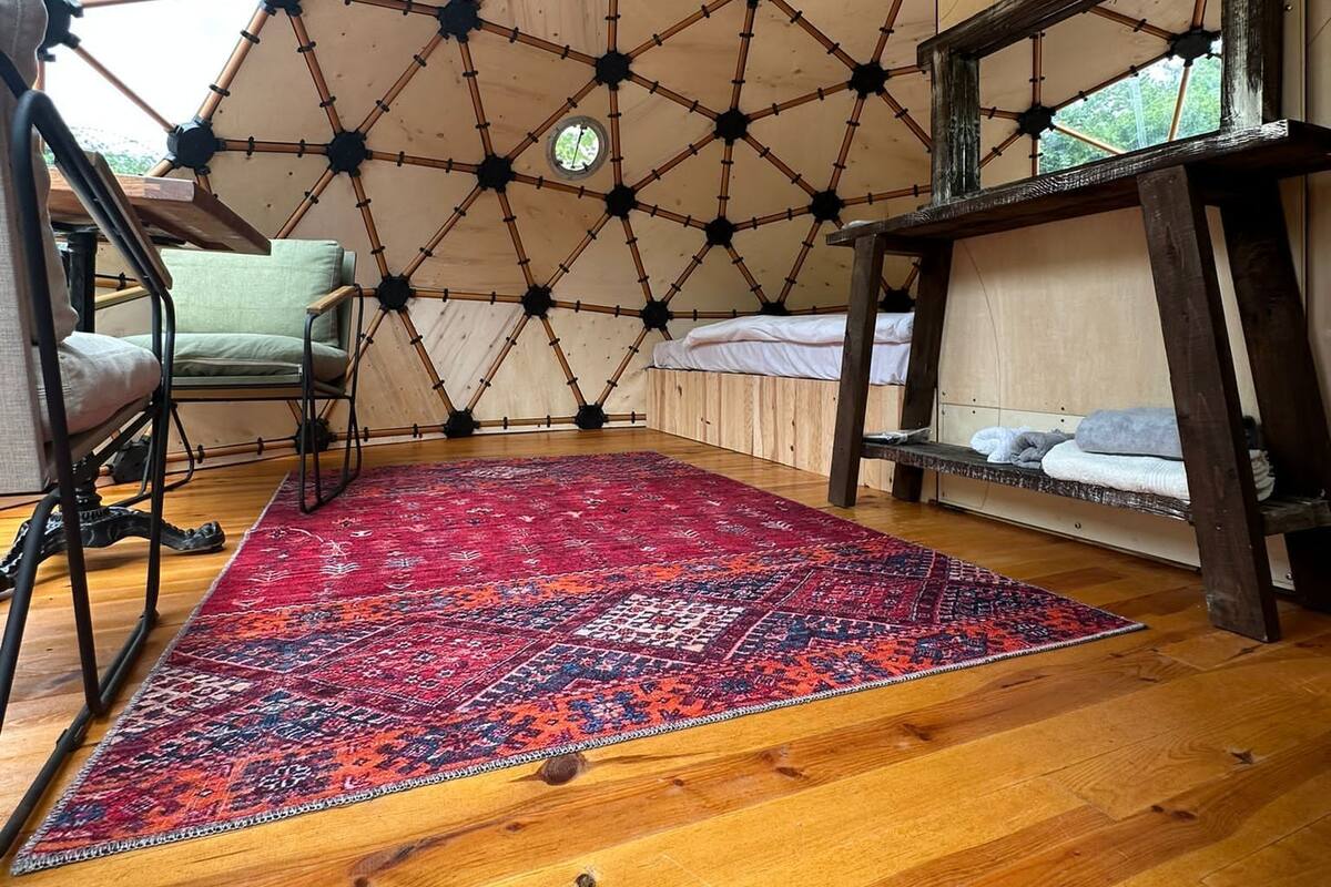 Uma estrutura em cúpula geodésica com piso de madeira e um tapete estampado.