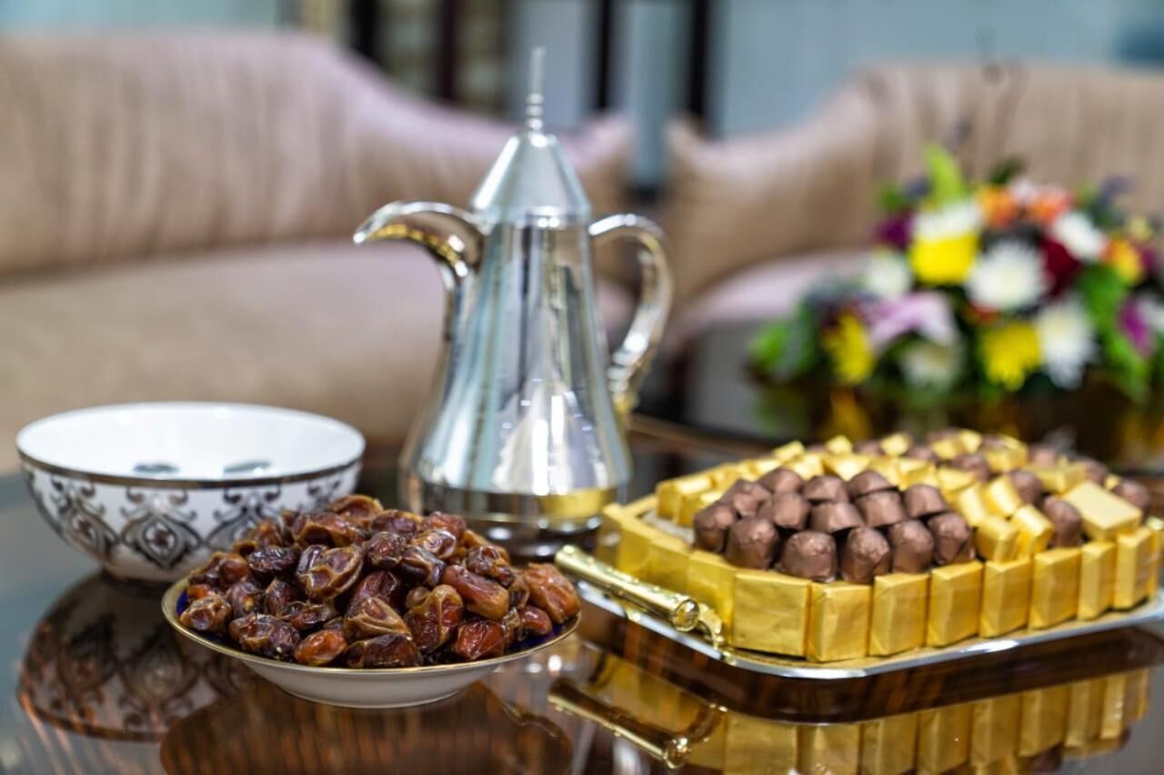 Una mesa con una tetera de plata, un cuenco de dátiles y una bandeja de dulces cubiertos de chocolate.