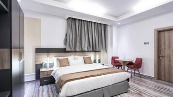 Una habitación de hotel moderna con una cama grande, mesitas de noche, un escritorio con sillas y un armario.
