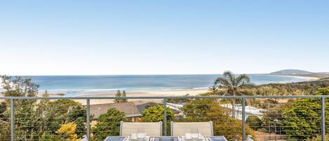 A dining area with a table set for two, overlooking a beach and ocean.