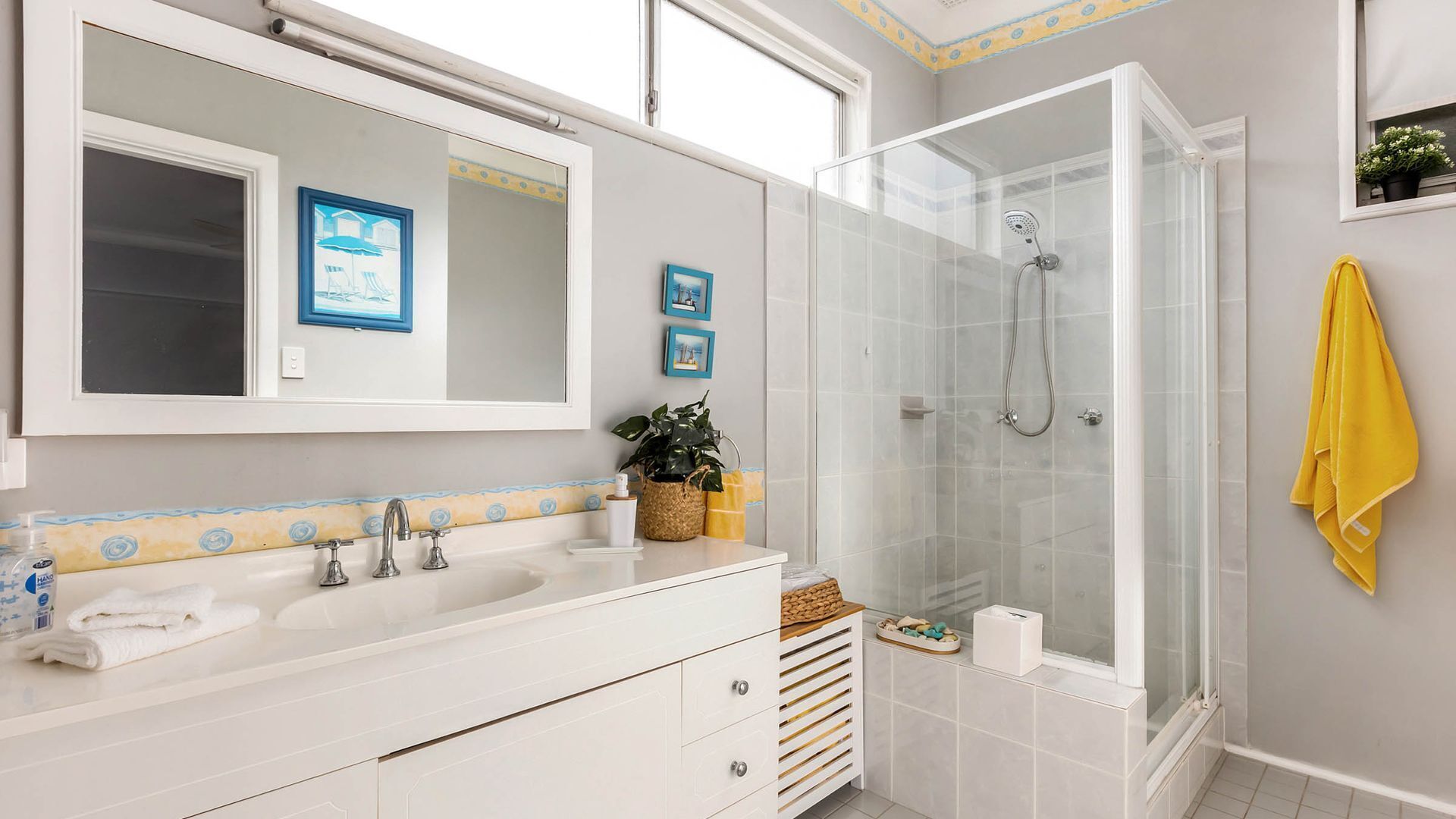 A bathroom with a double sink, a large mirror, a shower enclosure, and a yellow towel on the wall.