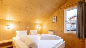 A wooden cabin bedroom with a bed, a window, and a wall-mounted picture.