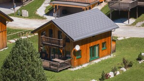 A wooden cabin with a balcony, a satellite dish, and a green door.
