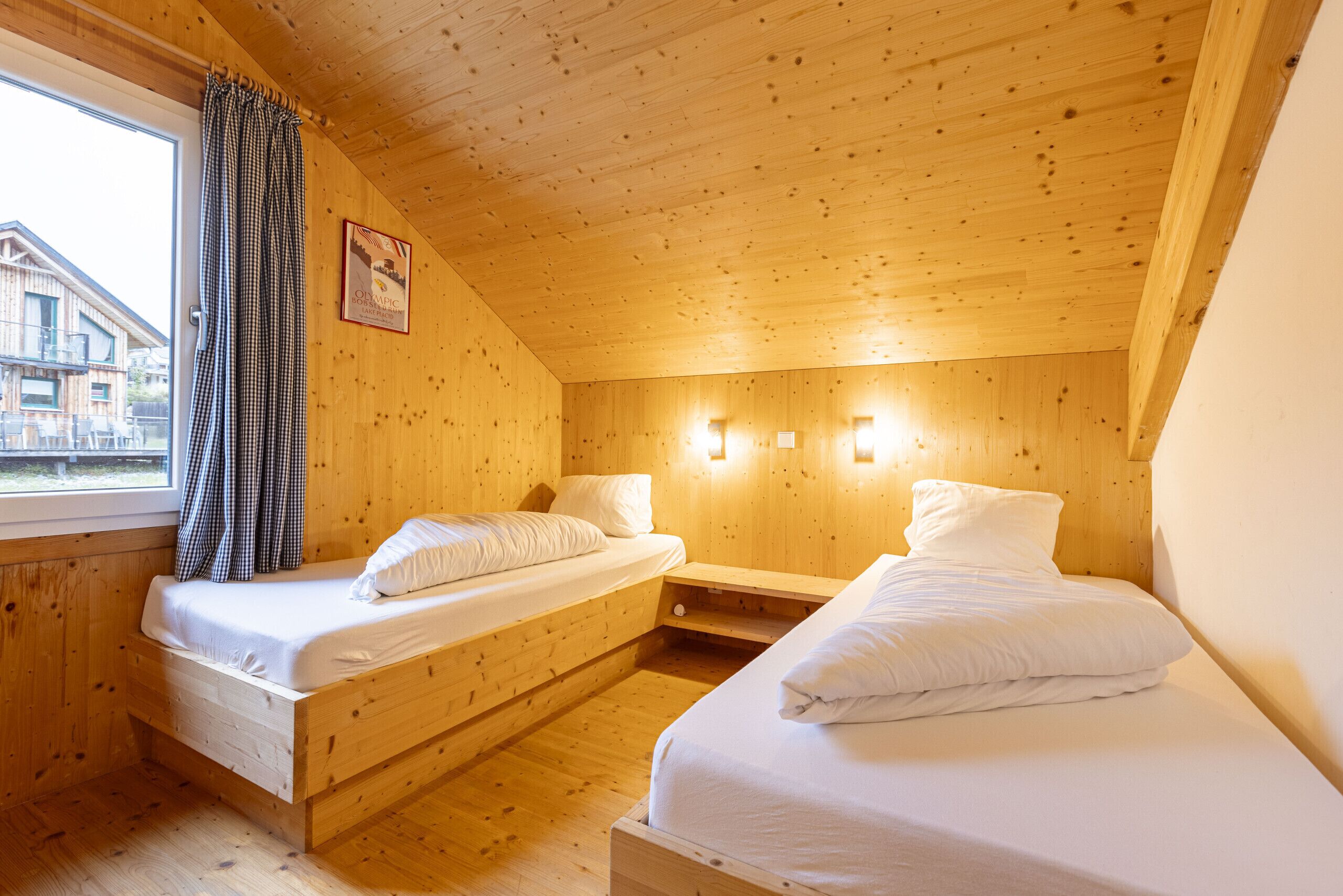 Een houten kamer met twee bedden, een raam met gordijnen en een lijst met een foto aan de muur.