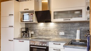 A modern kitchen with white cabinetry, a stainless steel range, a built-in microwave, and a wooden backsplash. - Superior Chalet # 61 with IR-Sauna (Hohentauern)