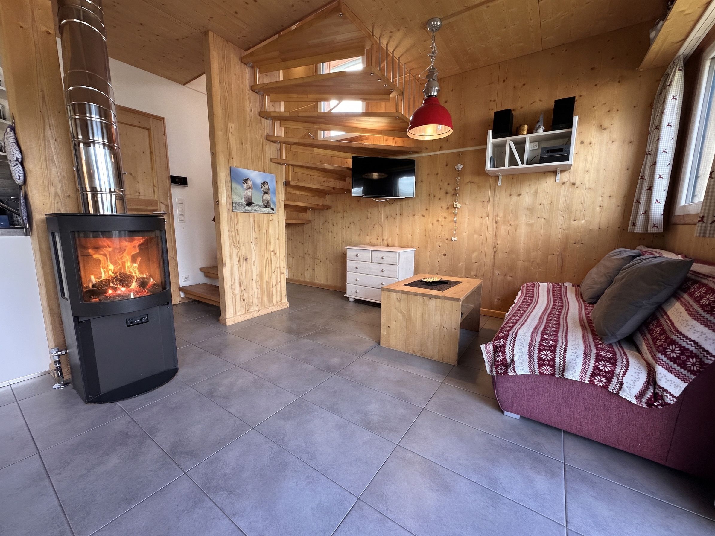 Un salon chaleureux avec un poêle à bois, un canapé, une table basse et un téléviseur fixé au mur.