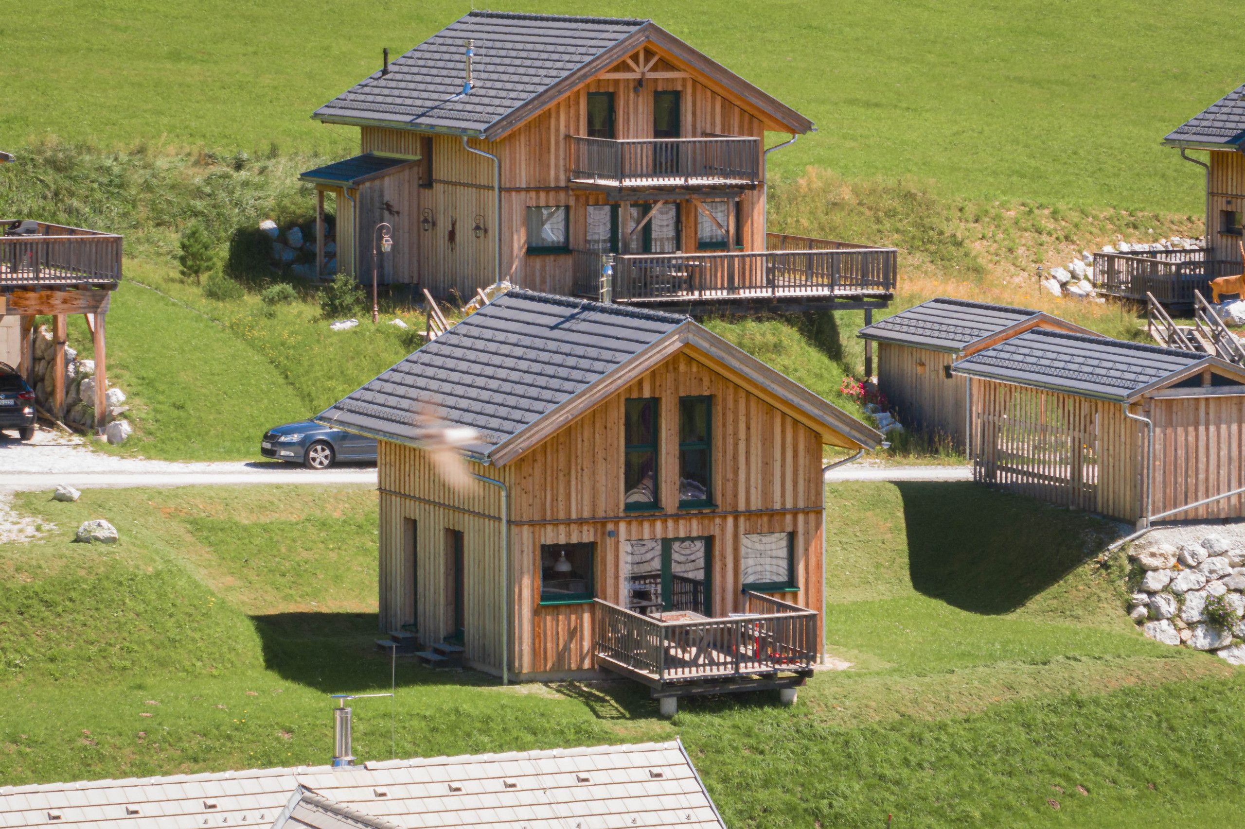 A cluster of wooden cabins with balconies, set in a grassy area with a clear sky.