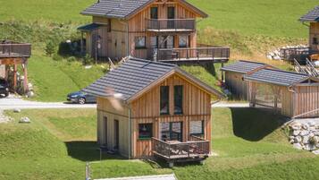 A cluster of wooden cabins with balconies, set in a grassy area with a clear sky.