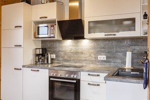 Cozinha moderna com armários brancos, fogão de aço inoxidável, micro-ondas embutido e painel de madeira.