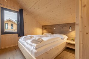 Dormitorio de una cabaña de madera con una cama, un ventanal y vistas a otra cabaña.