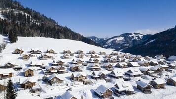 A snow-covered village with wooden cabins, surrounded by mountains and trees.