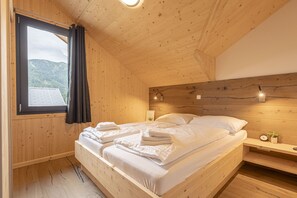 A wooden room with a bed, a nightstand, a clock, and a window with curtains.