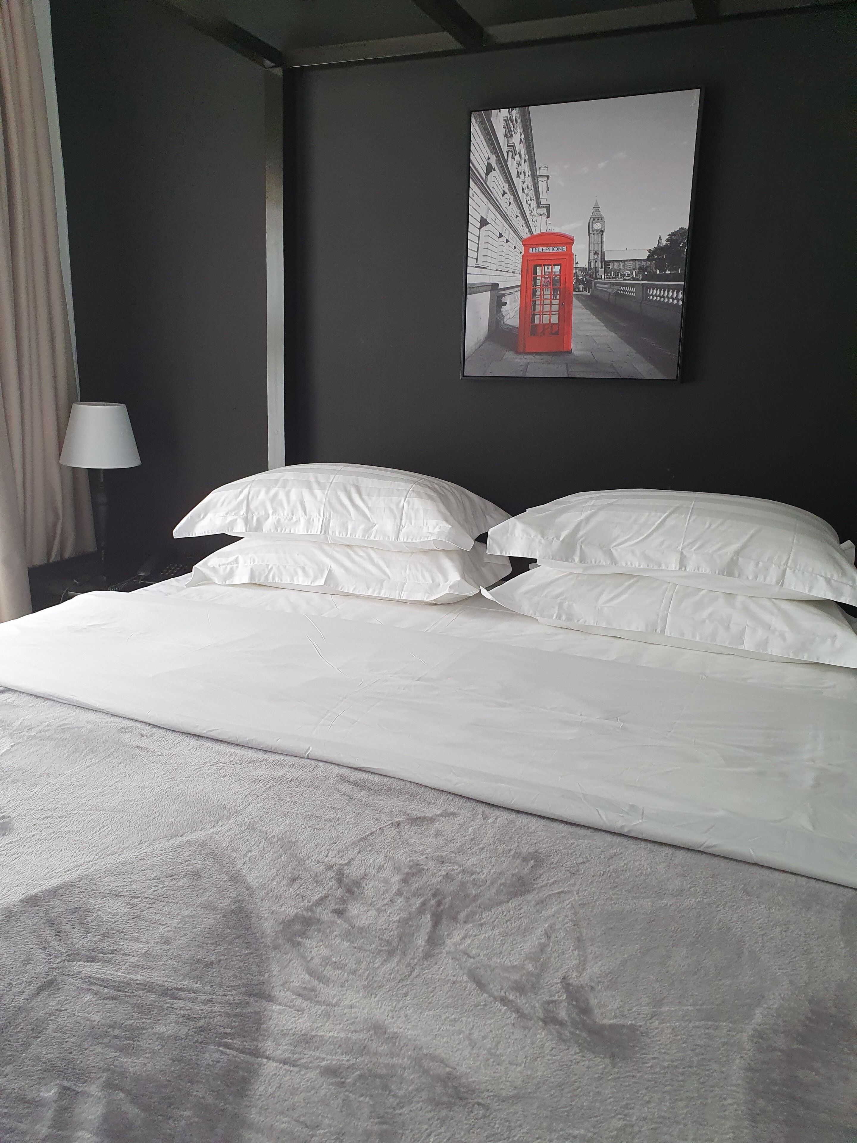 A hotel room with a large bed, a lamp, and a picture of a red telephone booth on the wall.