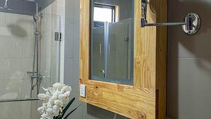 A bathroom with a wooden vanity, a white sink, a mirror, and a shower. - Bamboo Boutique (Lilongwe)