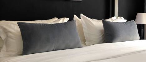 Una habitación de hotel con una cama grande, ropa de cama blanca y una pared negra.