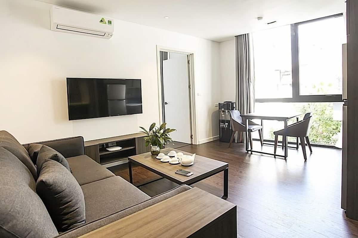A modern living room with a sofa, a coffee table, a TV, and a dining area with chairs and a table.