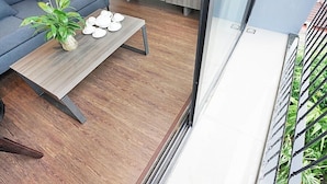 En moderne stue med en grå sofa, et træbord med pynteting, og udsigt til en balkon med gelænder.