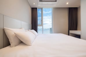 A hotel room with a large bed, a desk, and a view of a cityscape through a window. - Ocean Park 9 (Incheon)
