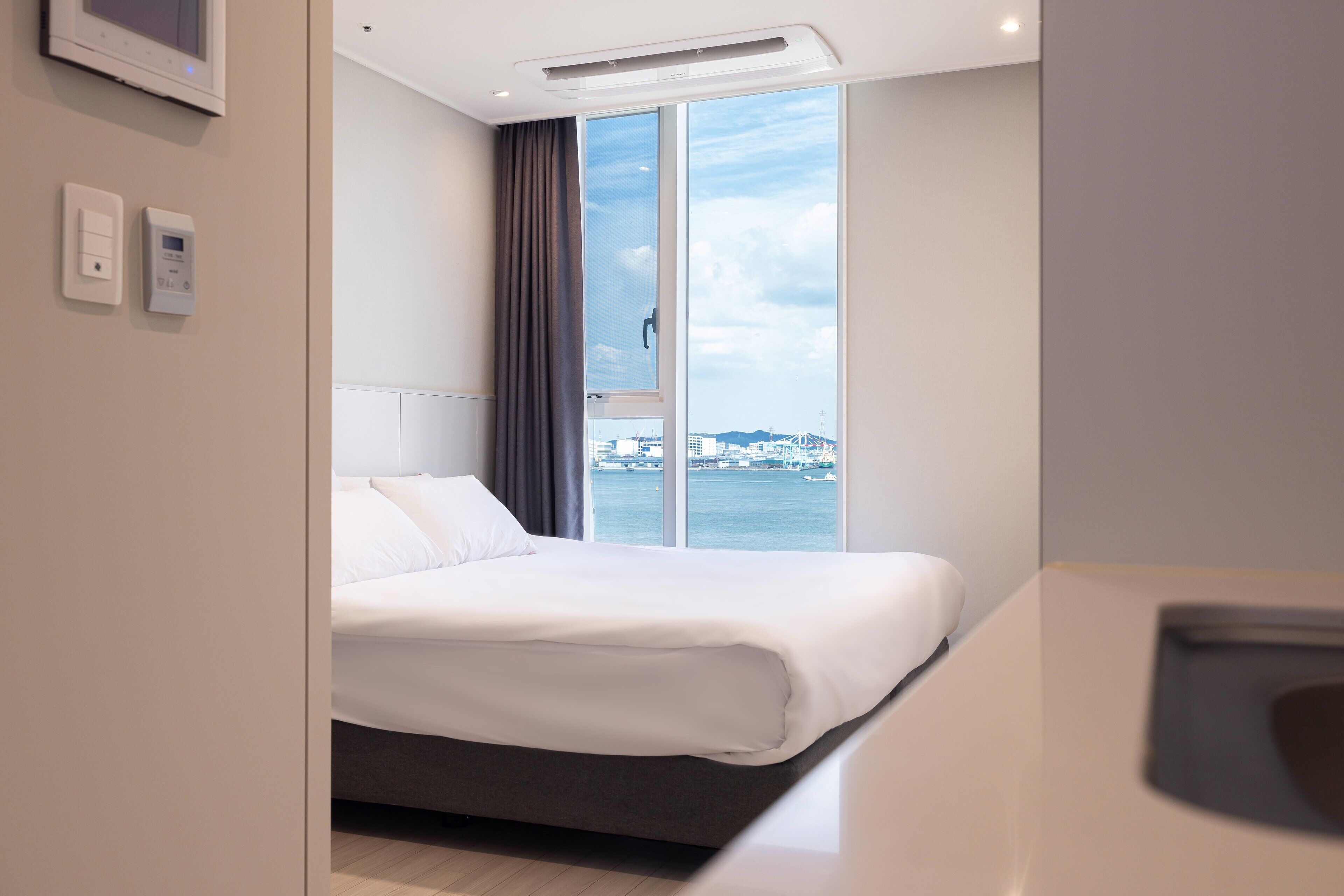 A modern hotel room with a large bed, a view of the sea, and a window with curtains.