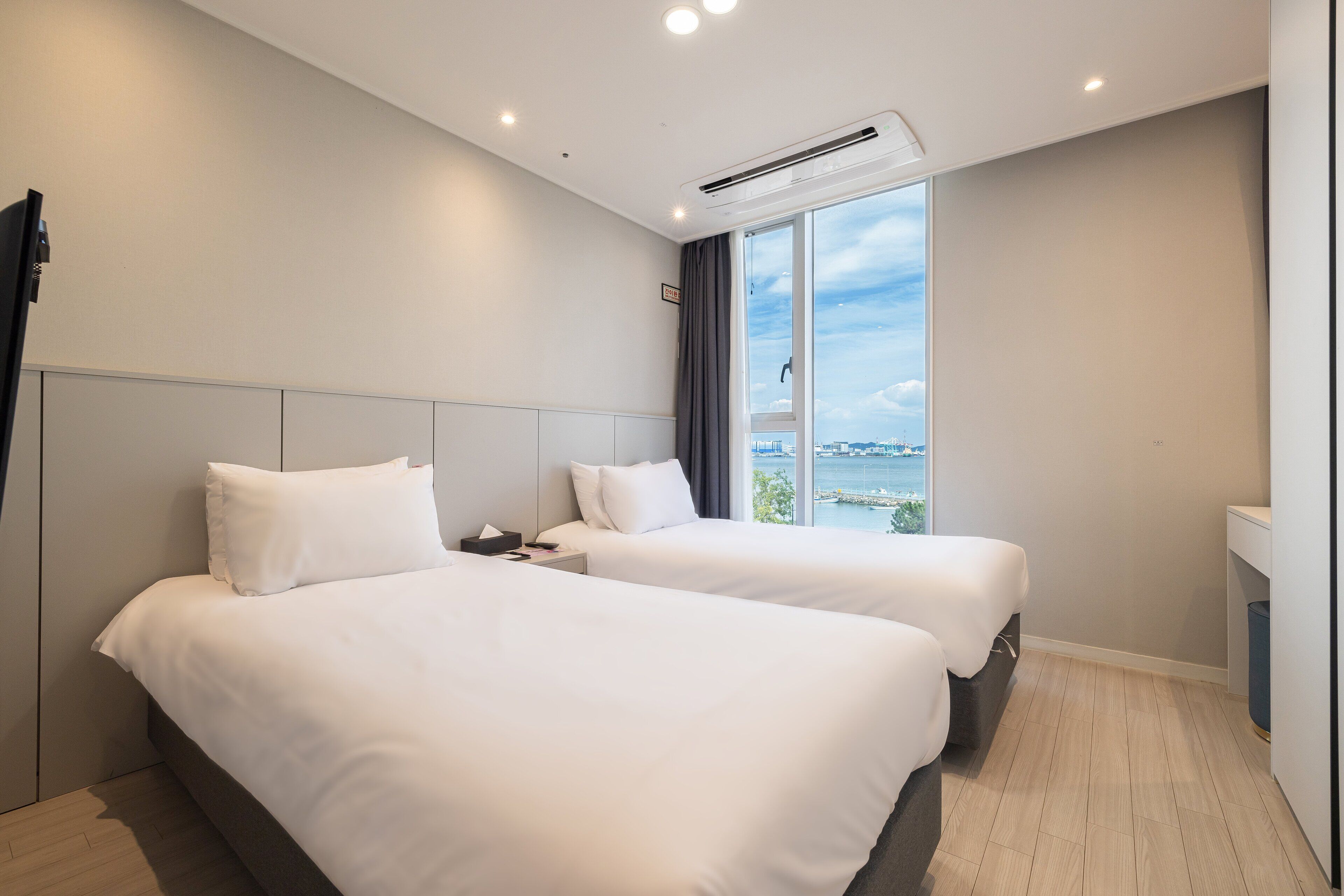Une chambre d’hôtel avec deux lits, une grande fenêtre donnant sur un beau paysage, une table de chevet et un appareil de climatisation.