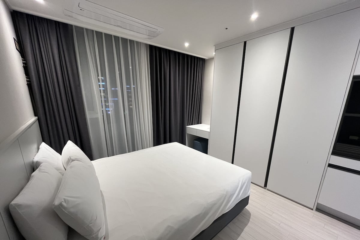 A modern hotel room with a large bed, a bedside table, a wardrobe, and a window with curtains.