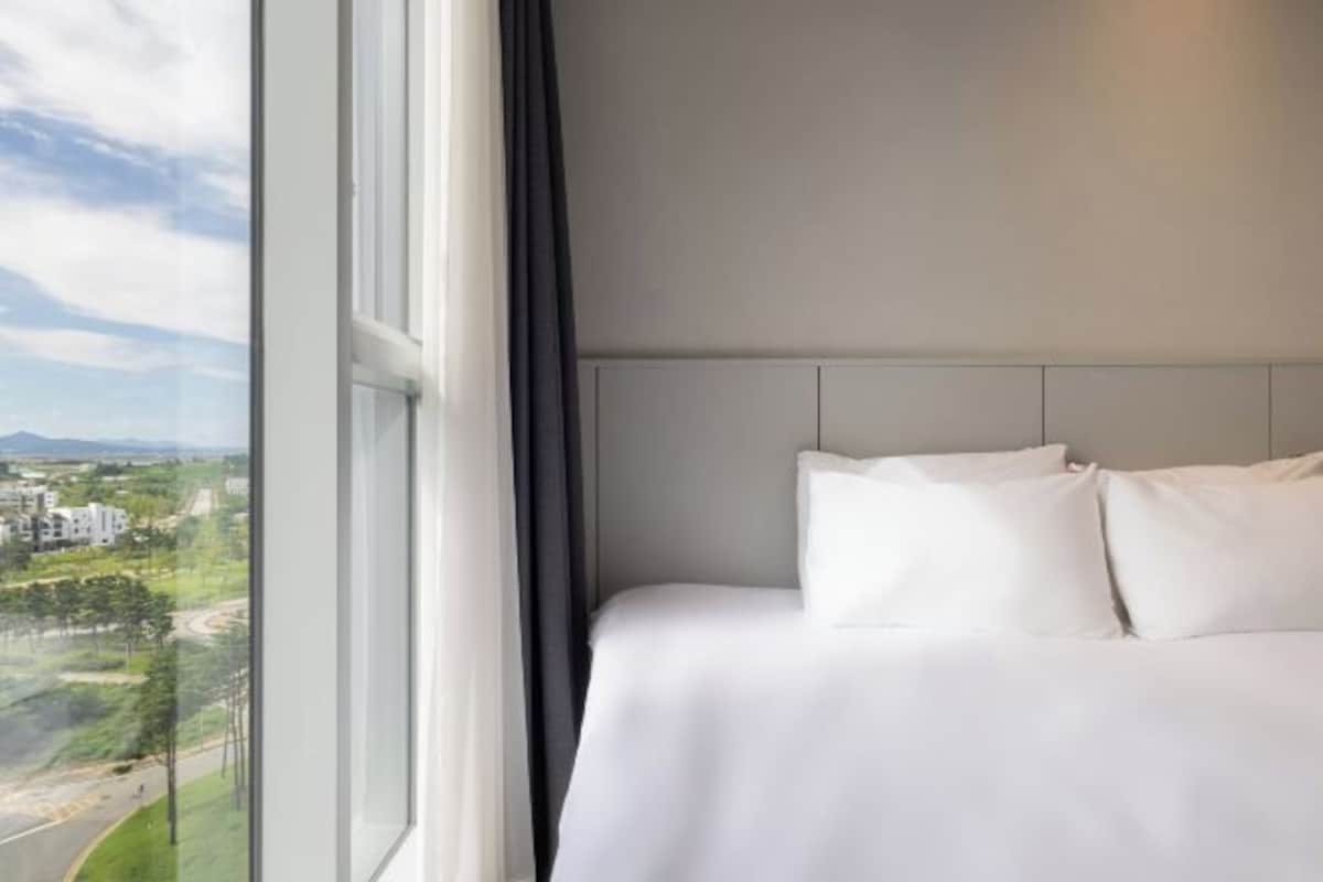 Habitación de hotel con un ventanal grande que ofrece vistas a un paisaje urbano y zonas verdes.