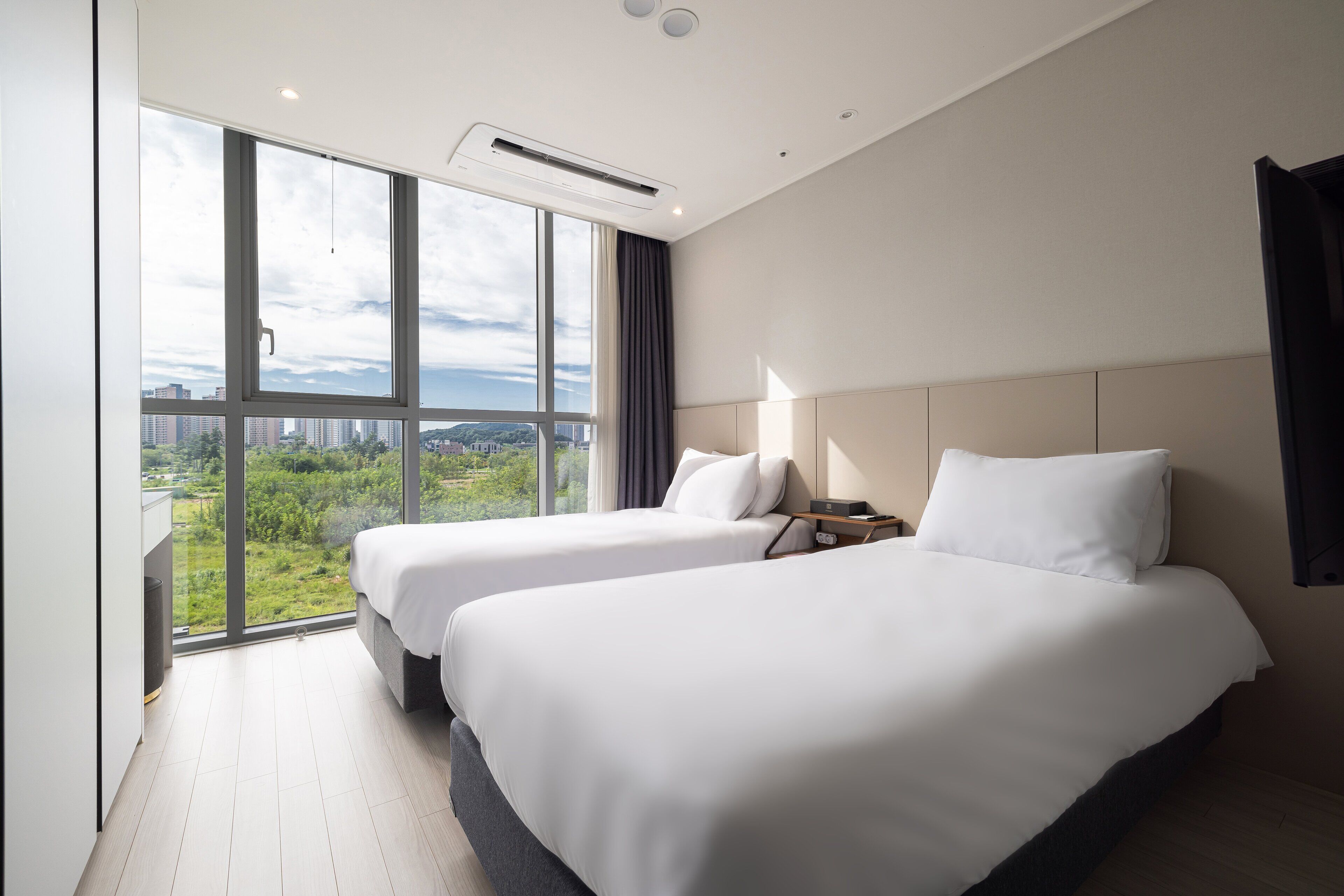 A hotel room with two beds, large windows, and a view of a cityscape.