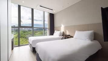 Habitación de hotel con dos camas, ventanas amplias y vistas a un paisaje urbano.