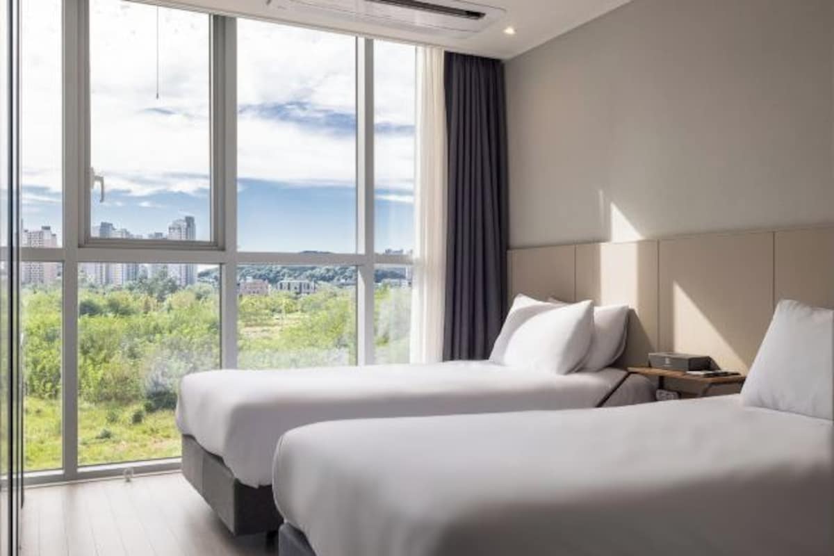 Habitación de hotel con dos camas, un ventanal amplio con vistas a la ciudad y un diseño moderno.