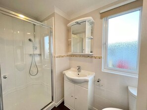 A bathroom with a glass-enclosed shower, a sink with a mirror above it, and a window providing a view of the outside. - Modern House in Carlisle Close to Lake District (Carlisle)