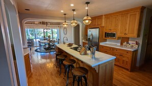 Una cocina moderna con armarios de madera, una isla central con taburetes, un refrigerador y un microondas.