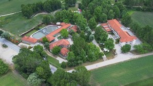 Vista aérea de una propiedad con varias edificaciones, una piscina y campos verdes circundantes.
