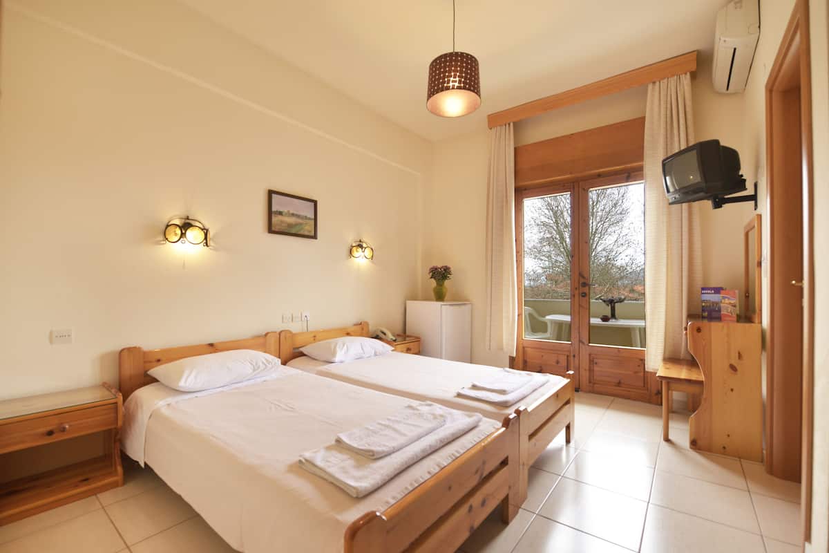 A hotel room with two wooden beds, a small desk, a television mounted on the wall, and a window with curtains.