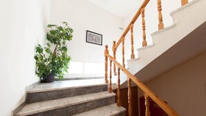 Una escalera con escalones de mármol y balaustres de madera, que conduce a un rellano con una planta en maceta y un cuadro en la pared.