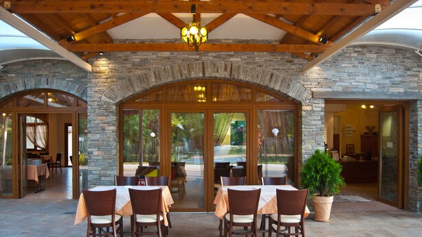 Un patio al aire libre con muros de piedra, vigas de madera y mesas dispuestas para comer.